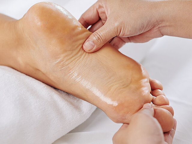 Fußreflexzonenmassage – Hände behandeln entspannt liegende Füße.